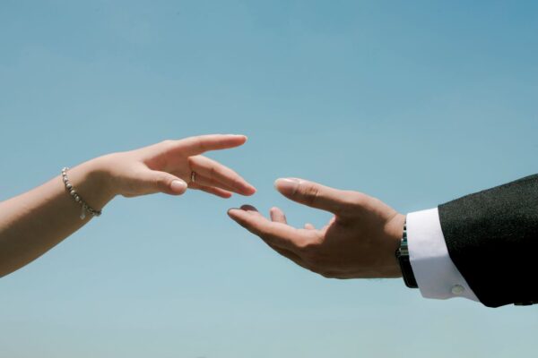 Close-up of two hands reaching towards each other under a clear blue sky, symbolizing connection.